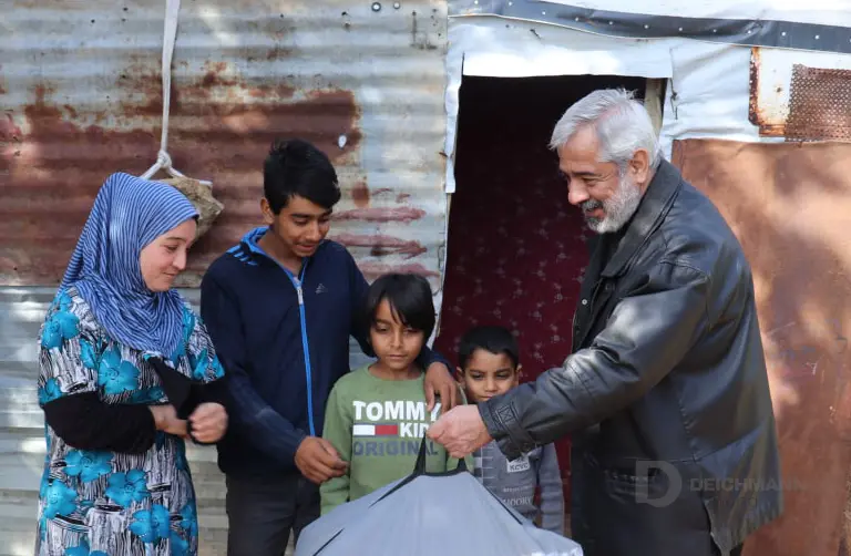Family receives aid delivery in front of temporary shelter