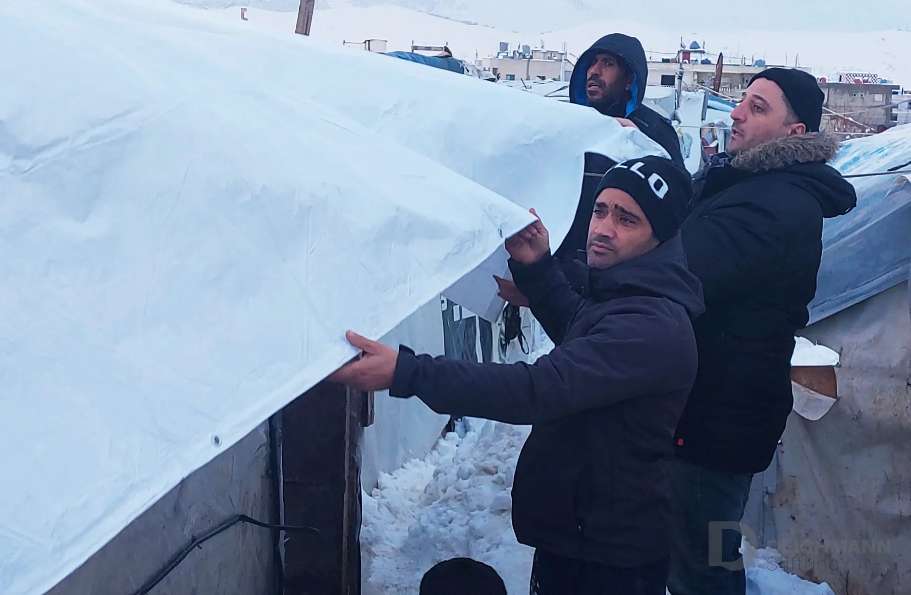 Men protect temporary shelter from snowfall with tarpaulin